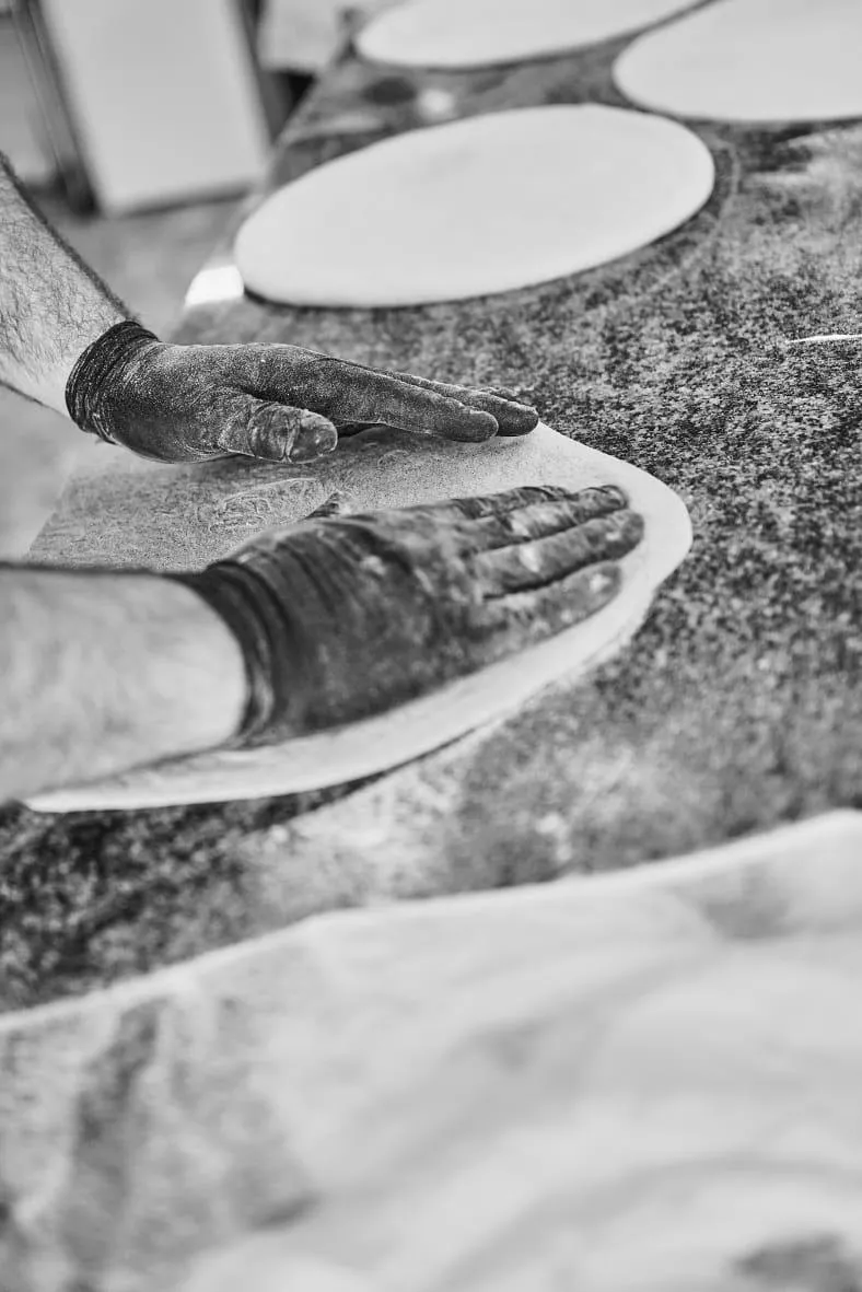 Le mani del pizzaiolo stendono l'impasto